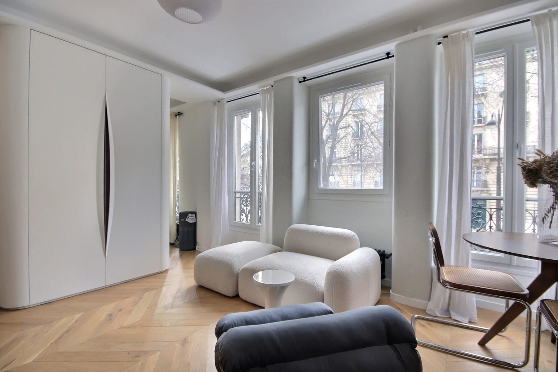 Séjour en parquet à chevrons avec rangements toute hauteur et fenêtres sur balcon parisien