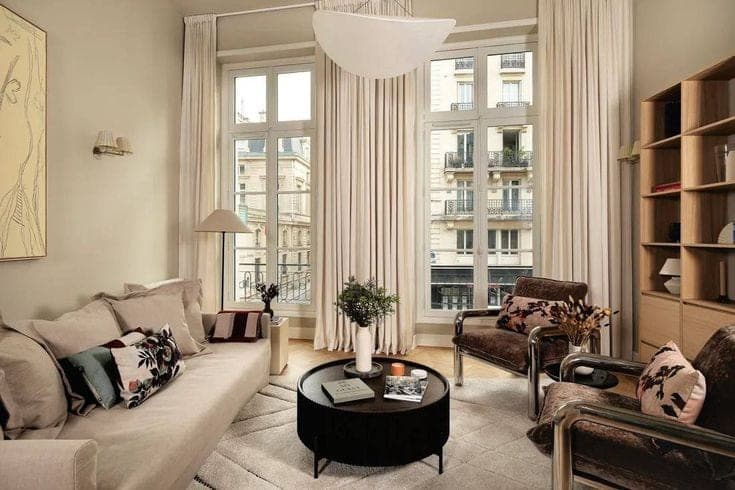 Séjour parisien sous haute hauteur, rideaux toute hauteur et fenêtres sur immeubles haussmanniens