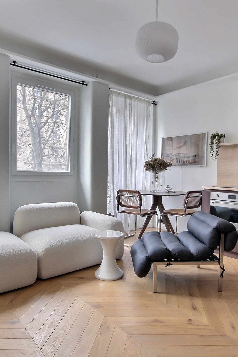 Séjour parisien lumineux avec canapé bouclé écru, parquet en point de Hongrie et balcon en fer forgé