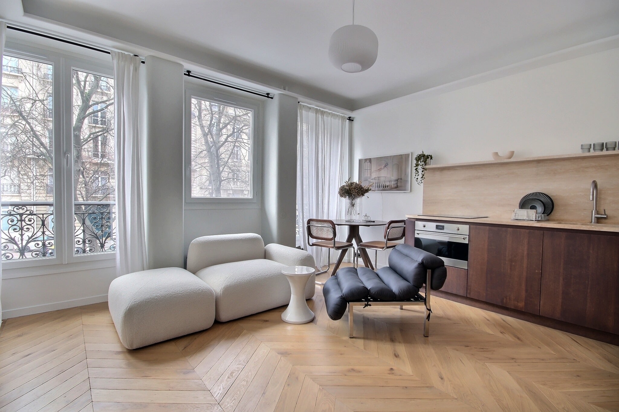 Séjour parisien lumineux avec canapé bouclé écru, parquet en point de Hongrie et balcon en fer forgé
