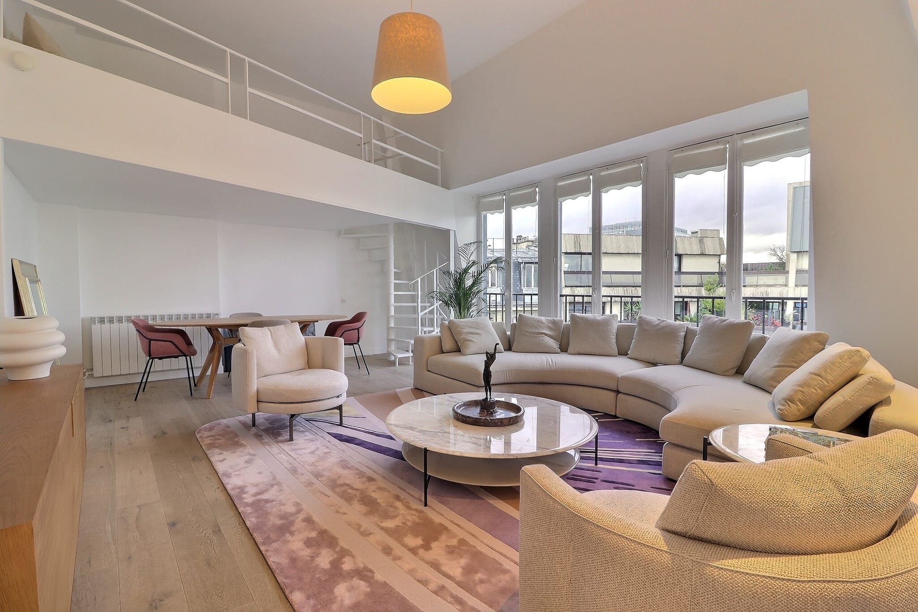 Séjour d’un duplex parisien avec mezzanine, canapé courbe et grandes fenêtres sur les toits